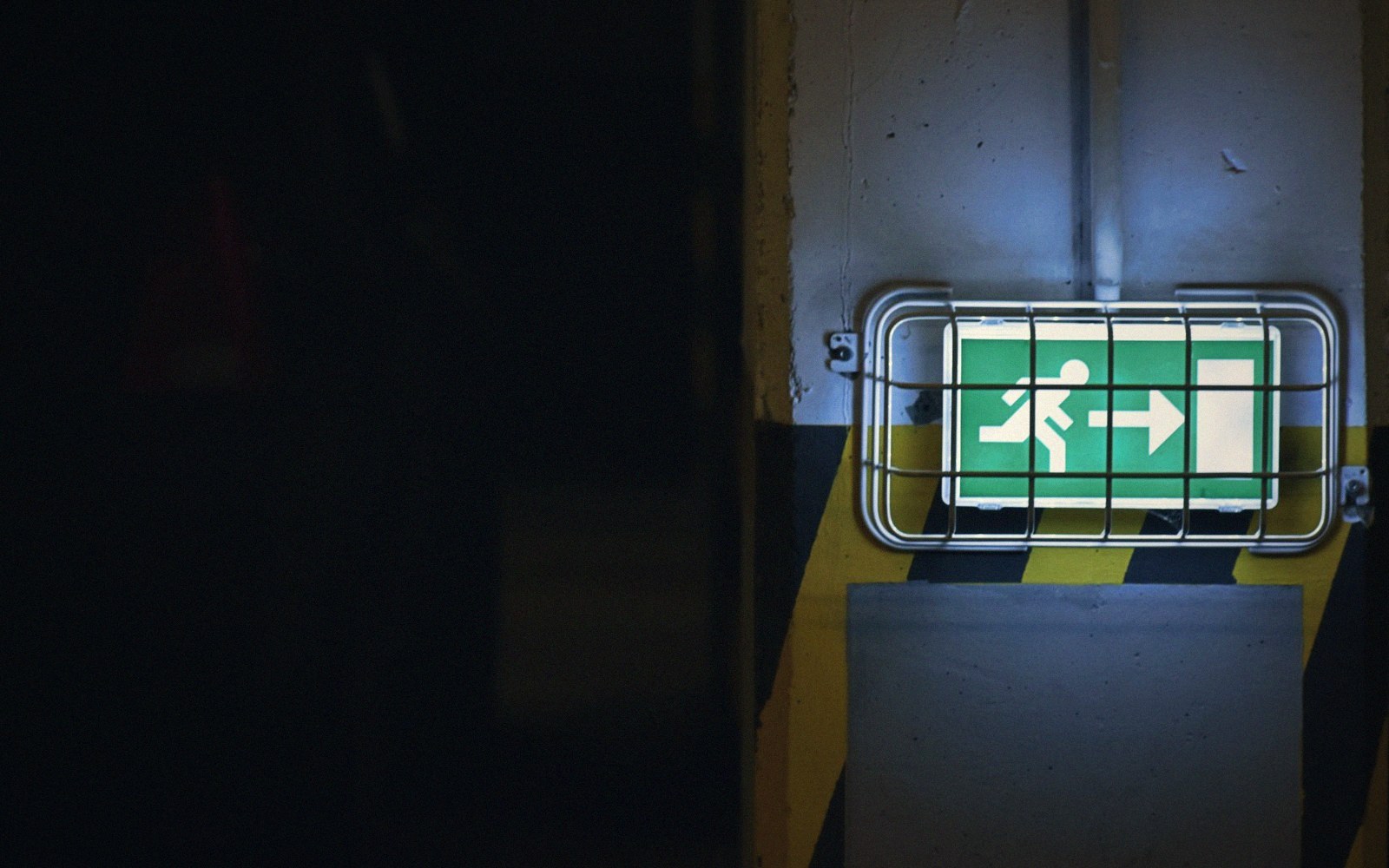 A green-lit EXIT sign glowing at the end of a dark cinema corridor, the floor reflecting its light