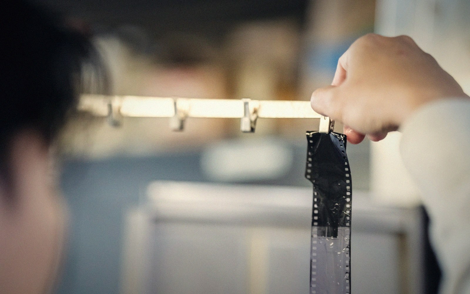 A hand clips a strip of developed 35mm film onto a drying line