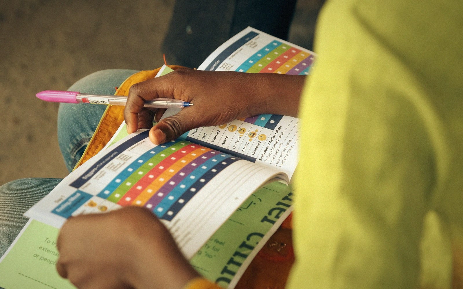 A child holds a pen while filling in a colorful mood-tracking worksheet