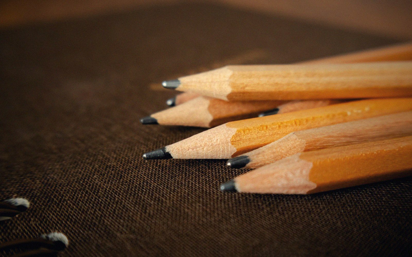 Sharpened wooden pencils with their tips resting on a dark fabric-covered notebook