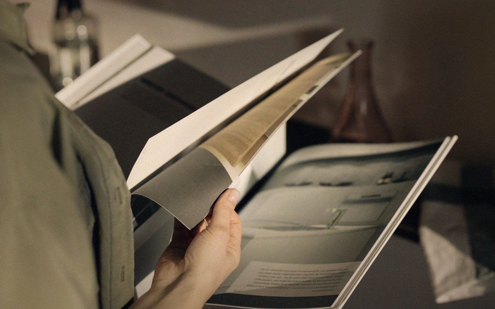 A hand turns a page of a large photography book with muted tones