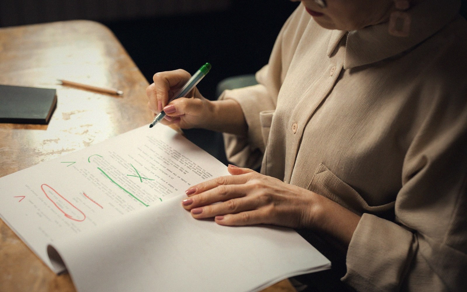 A person marks corrections in green and red ink on a handwritten page