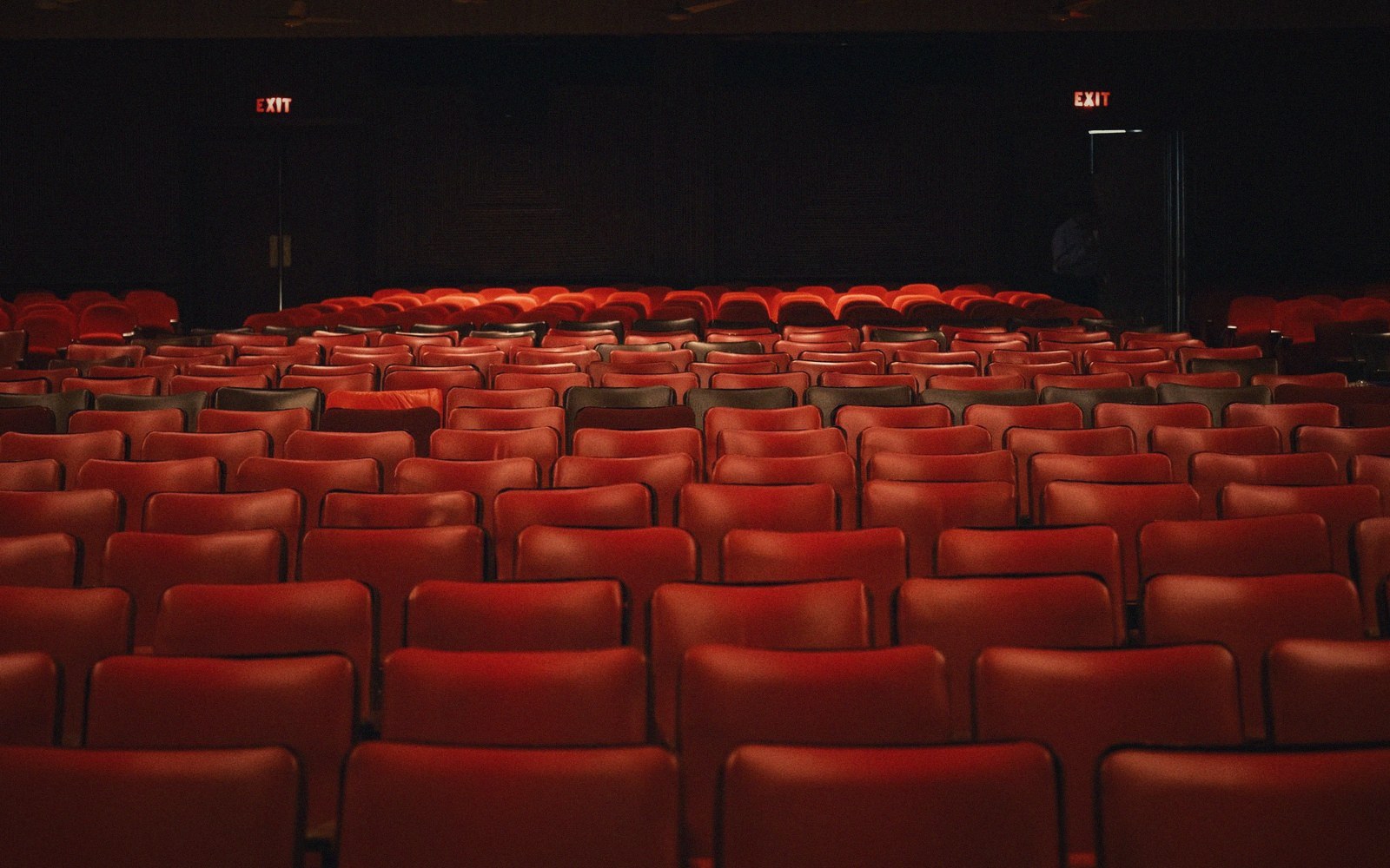 Rows of empty red seats in a darkened theater with illuminated exit signs