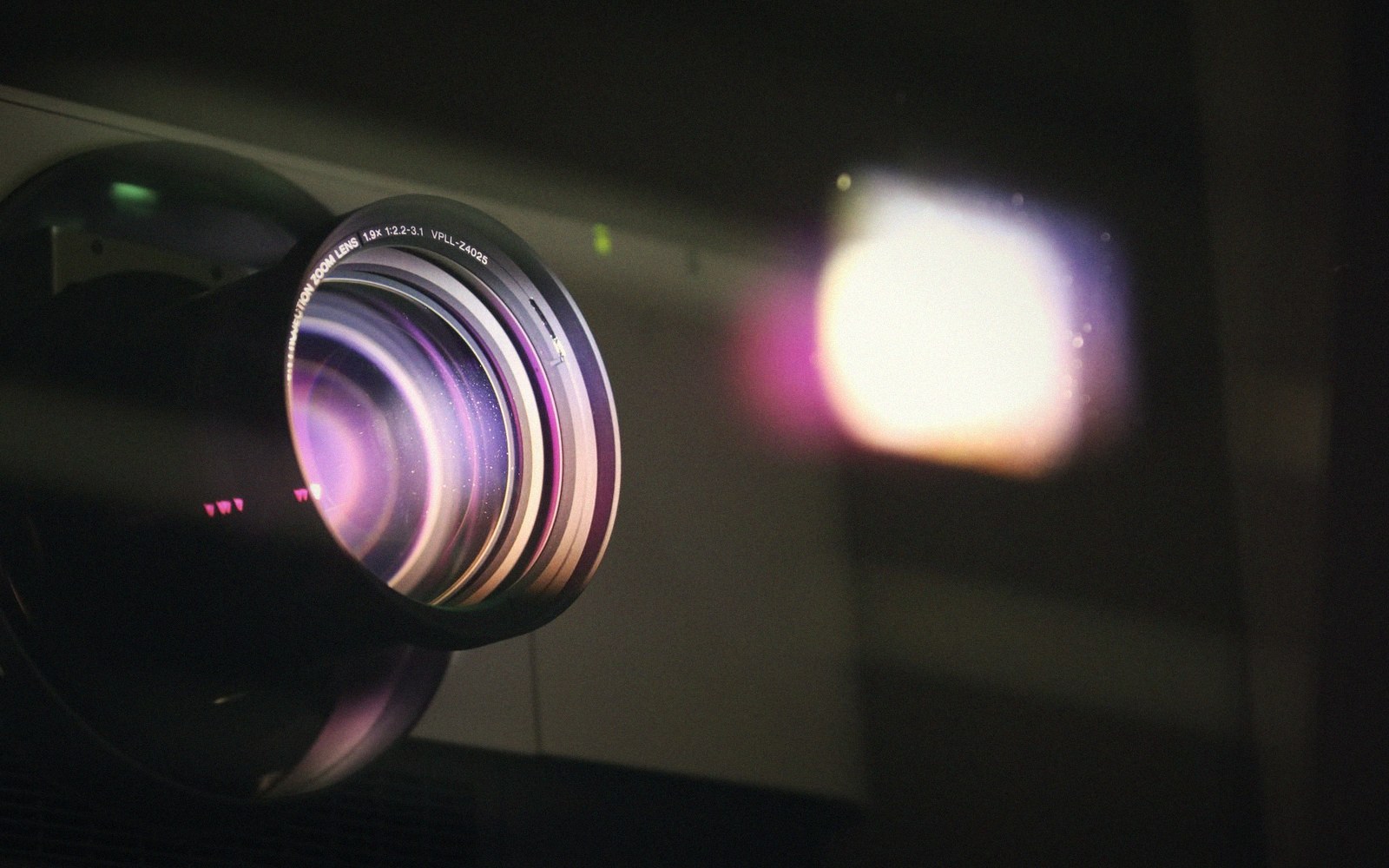 A cone of white projection light cutting through the dark above an unseen audience in a cinema auditorium